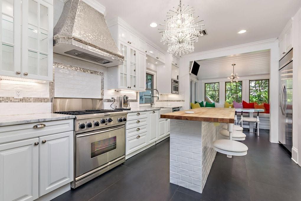 Finished white kitchen with a mosaic tile range hood, marble counters, and a butcher-block island with swivel stools